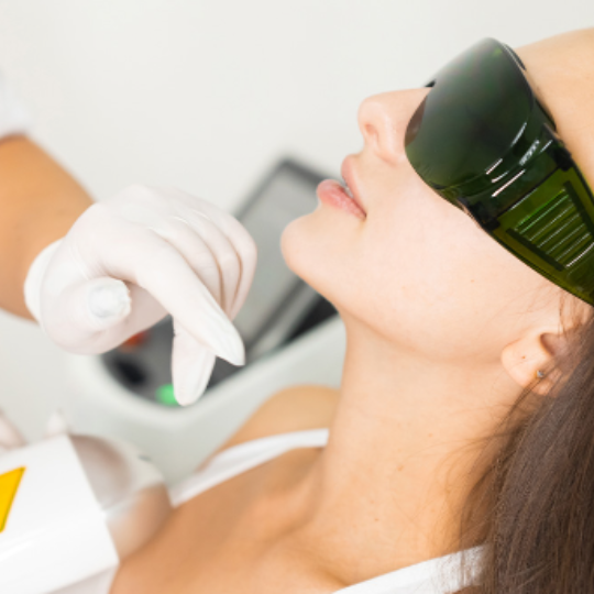 A person receiving laser hair removal treatment on their face, wearing protective eye goggles.
